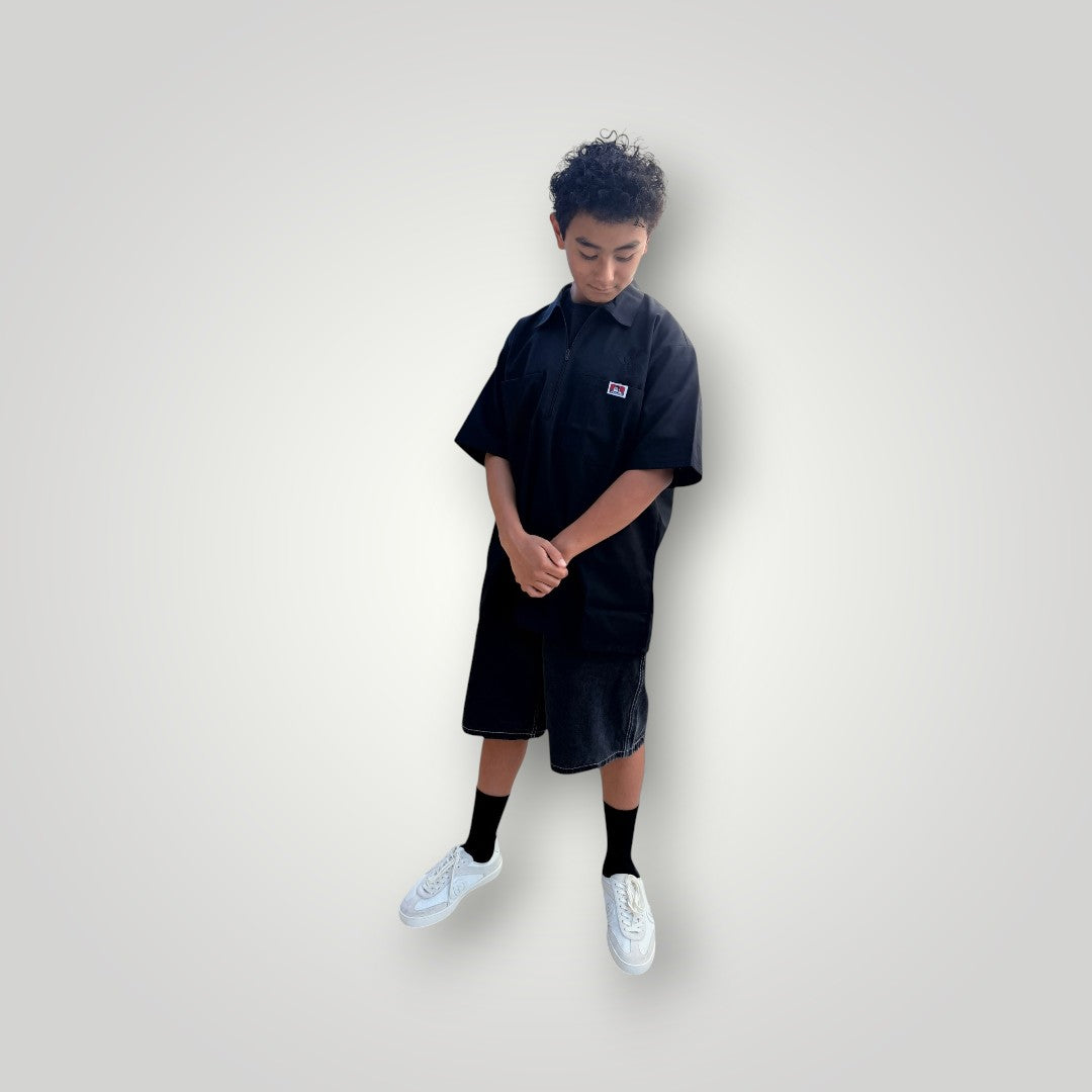 KA'EO x Ben Davis black poly-cotton twill work shirt with quarter-zip and chest pockets. Model is wearing shorts and sneakers.