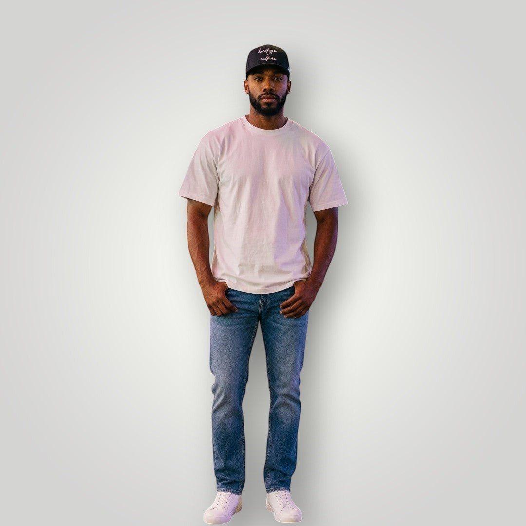 KA'EO Apparel black cotton baseball cap with embroidered "heritage + culture" text and KA'EO logo on side. Model wears cap with white t-shirt and jeans.