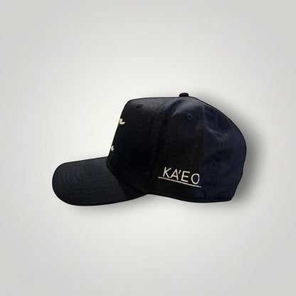 KA'EO Apparel black cotton baseball cap with embroidered "heritage + culture" script and side branding.