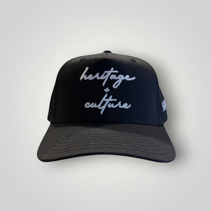 KA'EO Apparel black cotton snapback cap with embroidered 'heritage + culture' text and curved brim.