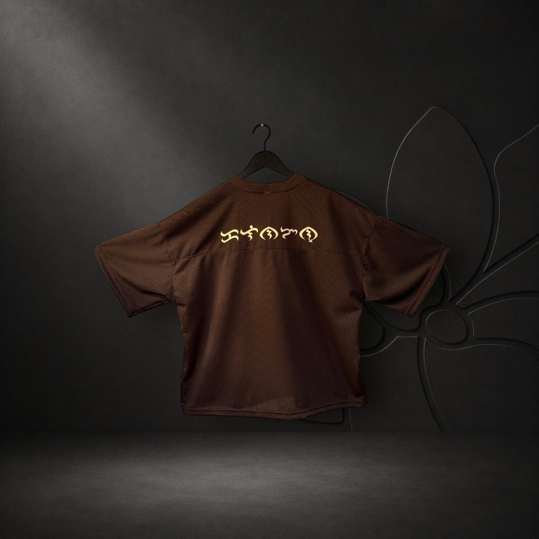 KA'EO Apparel brown mesh cropped football jersey with gold Baybayin script on the back, hanging against a dark background.