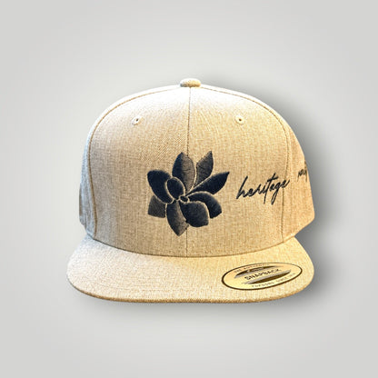 KA'EO Apparel heathered tan snapback hat with embroidered dark gray sampaguita flower and "heritage + culture" script.