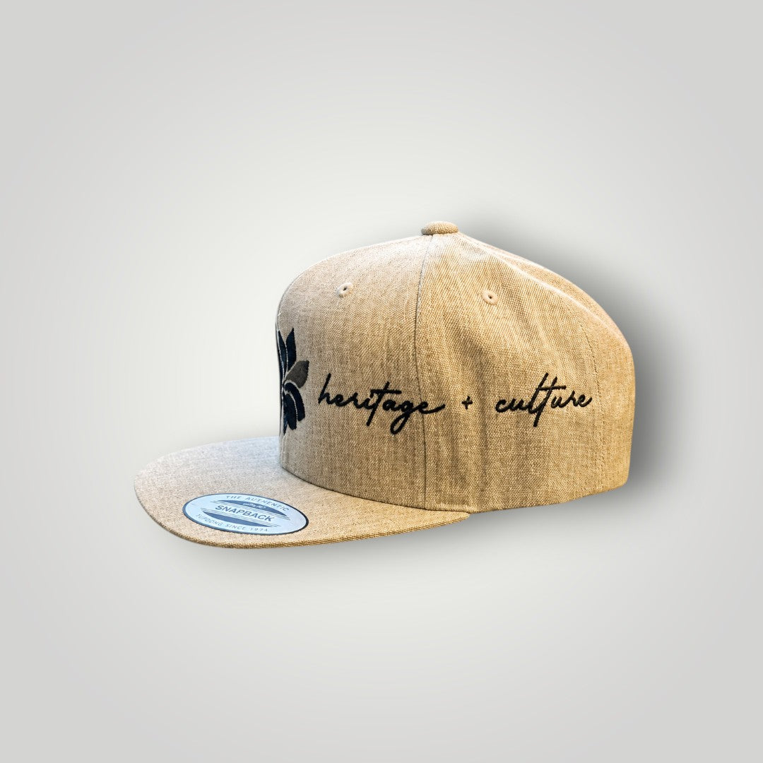KA'EO Apparel heathered tan snapback hat with embroidered dark gray sampaguita flower and "heritage + culture" script.