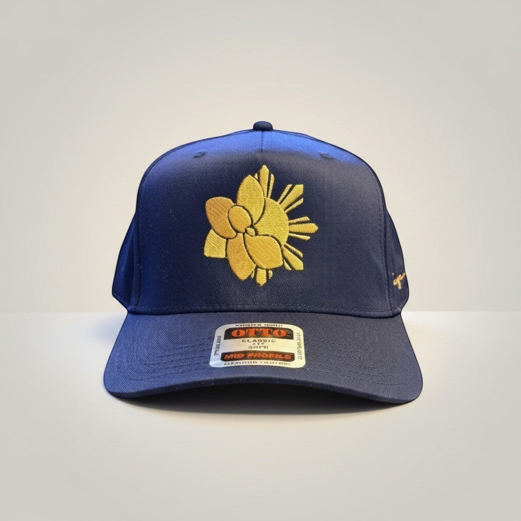 KA'EO Apparel navy blue snapback hat with gold embroidered Sampa-Sol symbol and "heritage + culture" script.